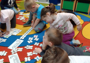 Dzieci na dywanie układają z elementów trasy dla robotów.