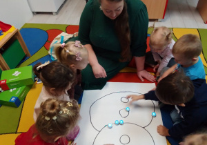 Dzieci i z biblioteki obserwują Ozoboty podążające trasą w kształcie bałwana.