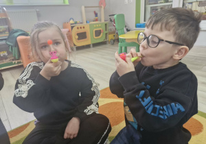 Weronika i Antoś wykonują ćwiczenia oddechowe z wykorzystaniem logopedycznych dmuchajek.