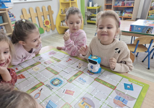 Na stoliku leży plansza i robot do nauki kodowania. Ala ogląda robota Doc.