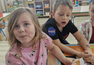 Weronika i Franek siedzą przy stoliku, dzieci trzymają w dłoniach karty do kodowania.