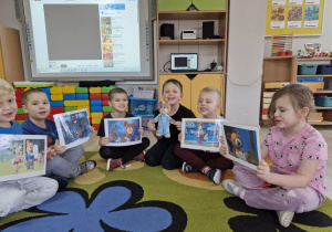Przedszkolaki trzymają w dłoniach obrazki z wizerunkami głównych bohaterów bajki "Miś Uszatek".