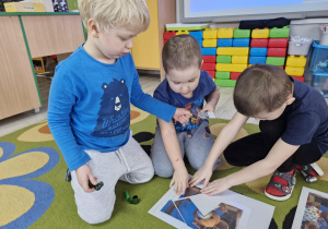 Karol, Szymon i Staś układają pocięty na części obrazek z wizerunkiem Misia Uszatka.