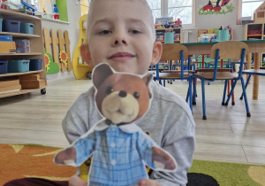 Lucjan siedzi na dywanie trzymając w dłoni obrazek z Misiem Uszatkiem.