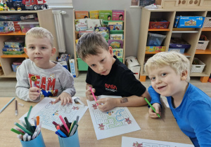 Lucjan, Franek i Karol siedzą przy stoliku, na którym widać karty pracy "Labirynty" z wizerunkami misiów.