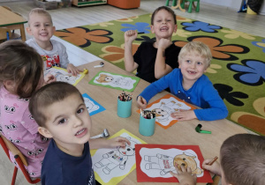 Dzieci siedzą przy stoliku w trakcie wykonywania pracy plastycznej.