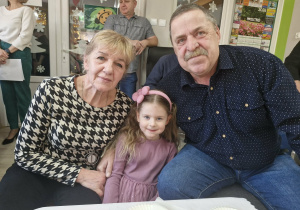 Oleńka siedzi przy stoliku w towarzystwie swoich dziadków.