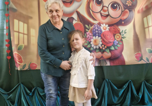 Weronika ze swoją babcią pozują do zdjęcia na tle dekoracji.