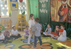 Weronika i Antoś tańczą na środku dywanu. W tle siedzą pozostałe dzieci, które śpiewają piosenkę dla swoich babć i dziadków.