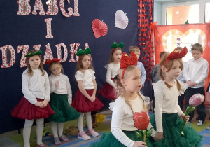 Tosia i Emma stoją na środku sceny i śpiewają piosenkę. Za nimi ośmioro dzieci stoi na tle dekoracji.