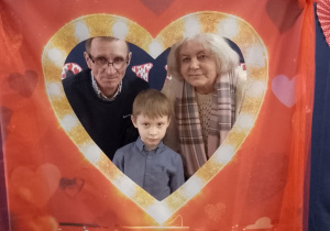 Adaś pozuje do wspólnego zdjęcia z Babcią i Dziadkiem w fotobudce.