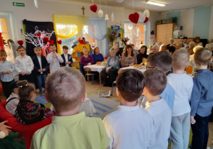 Babcie i Dziadkowie siedzą przy stołach i oglądają występ dzieci.