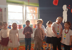 Grupa dzieci z panią Asią w trakcie śpiewania piosenki, za nimi na parapecie ustawione laurki.