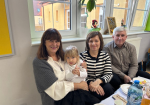 Emilka pozuje do zdjęcia ze swoimi babciami oraz dziadkiem.