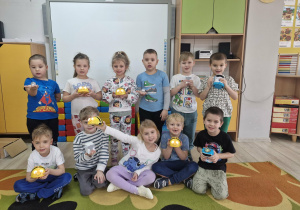 Dzieci stoją przed tablicą multimedialną. Każde dziecko trzyma jednego z robotów do nauki kodowania.