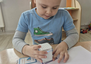 Oskar siedzi przy stole i przykłada Genibota do kart do kodowania.