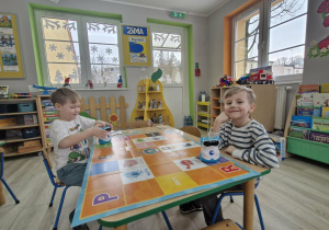 Wojtuś i Olek siedzą przy stole i programują DocRoboty na specjalnej macie do kodowania.