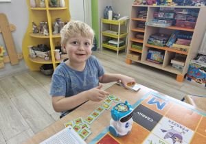 Karol siedzi przy stoliku i obserwuje jadącego po macie DocRobota.