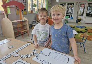 Ignacy i Karol obserwują Ozoboty jeżdżące po kartce papieru z narysowanym autkiem.