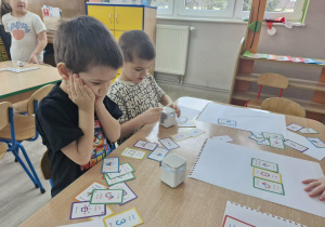 Wojtuś i Staś siedzą przy stoliku, na którym widać Geniboty i karty do kodowania.