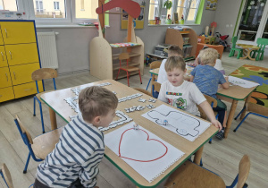 Olek i Wojtek obserwują Ozoboty jadące po kartkach papieru z narysowanymi serduszkiem i samochodem.