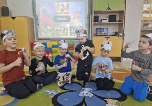 Dzieci siedzą na dywanie i wykonują ćwiczenia oddechowe z wykorzystaniem baniek mydlanych.