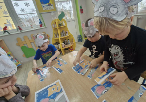 Przedszkolaki siedzą przy stoliku i układają obrazki z części z wizerunkami szarych gryzoni.