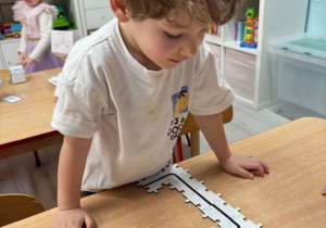 Michał spogląda na ułożone puzzle, po których jeździ ozobot.