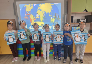 11. Dzieci stoją trzymając w dłoniach wykonane przez siebie prace plastyczne z wizerunkami dinozaurów.