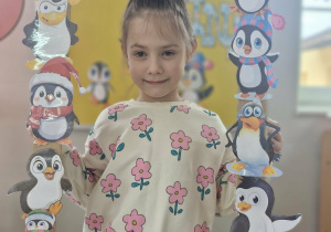 14. Oliwia trzyma w dłoniach foto-ramkę z wizerunkami pingwinów.