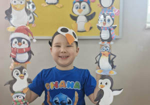 15. Szymek uśmiecha się do zdjęcia trzymając w dłoniach foto-ramkę z pingwinkami.