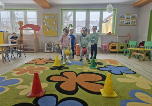 5. Na dywanie widać rozłożone pachołki. Dzieci z piłkami ułożonymi między kolanami udają pingwiny przenoszące jajka.