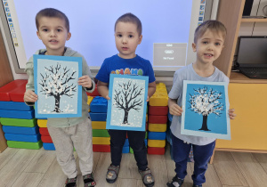 10. Dzieci stoją przed tablicą multimedialną i prezentują wykonane prace plastyczne.