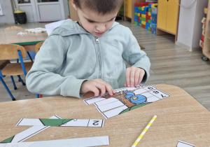 4. Staś siedzi przy stoliku i układa obrazek pocięty na części.