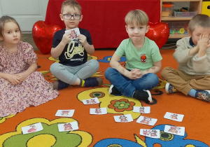 Franek siedzi na dywanie i prezentuje obrazek z walentynkowym misiem. Obok siedzi Felicja i dwóch kolegów.