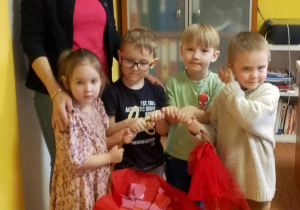 „Motylki” pozują do zdjęcia z Panią dyrektor podczas wręczania walentynkowych upominków. Dzieci trzymają koszyk, w którym znajdują się pudełeczka walentynkowe z niespodzianką.