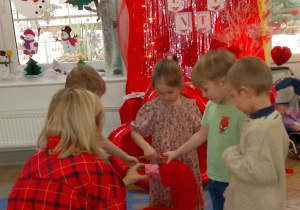 „Motylki’ wręczają „Walentynkę” Pani Monice. W tle dekoracja walentynkowa na sali „Słoneczek”.