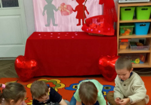 Dzieci układają na babeczkach serduszkową posypkę. W tle dekoracja walentynkowa.