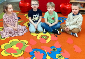 Dzieci siedzą obok siebie, a przed nimi leżą serduszkowe puzzle wycięte z papieru.