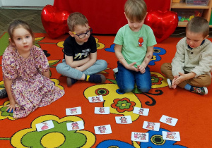 Dzieci siedzą na dywanie, a przed nimi leżą obrazki z walentynkowymi misiami.