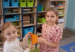 Marysia i Zuzia trzymają pomarańczowe serduszka.