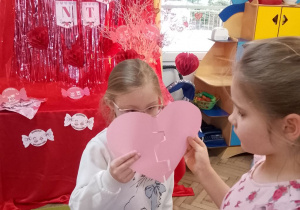 Marysia i Zuzia trzymają połówki różowego serca.