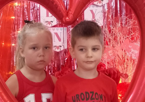 Tosia i Mikołaj pozują do zdjęcia w ramce balonowej w kształcie serca.