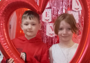 Emma i Antek pozują do zdjęcia w ramce balonowej w kształcie serca.