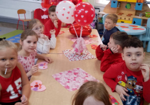 Dzieci siedzą przy wspólnym stole i spożywają serduszkowe lizaki.
