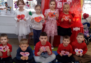 Zdjęcie grupowe dzieci z wykonanymi kartkami na tle dekoracji.