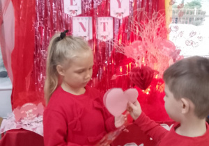 Tosia i Mikołaj wymieniają się kartkami walentynkowymi na tle dekoracji.