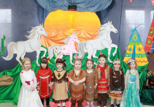 Dziewczynki z motylków pozują do zdjęcia. W tle galopujące konie.