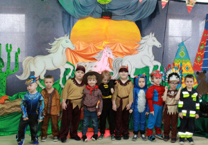 Chłopcy z motylków pozują do zdjęcia. W tle galopujące konie.