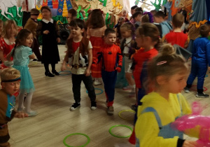 Przedszkolaki wskakują do kolorowych obręczy ułożonych na podłodze.